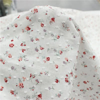 Le "Tissu plumetis rouge à motifs floraux au mètre" de Longan Craft France présente une texture pointillée vintage avec de petits motifs floraux rouges, roses et violets, parfaits pour des créations élégantes.