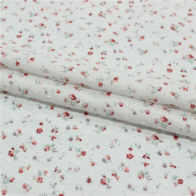 Gros plan sur le Tissu plumetis rouge à motifs floraux au mètre de Longan Craft France, un tissu de coton vintage aux imprimés floraux et à pois, présenté dans des plis délicats.