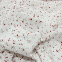 Un gros plan du Tissu plumetis rouge à motifs floraux au mètre de Longan Craft France montre un tissu vintage léger avec des motifs floraux et à pois, légèrement froissé pour un aspect charmant.