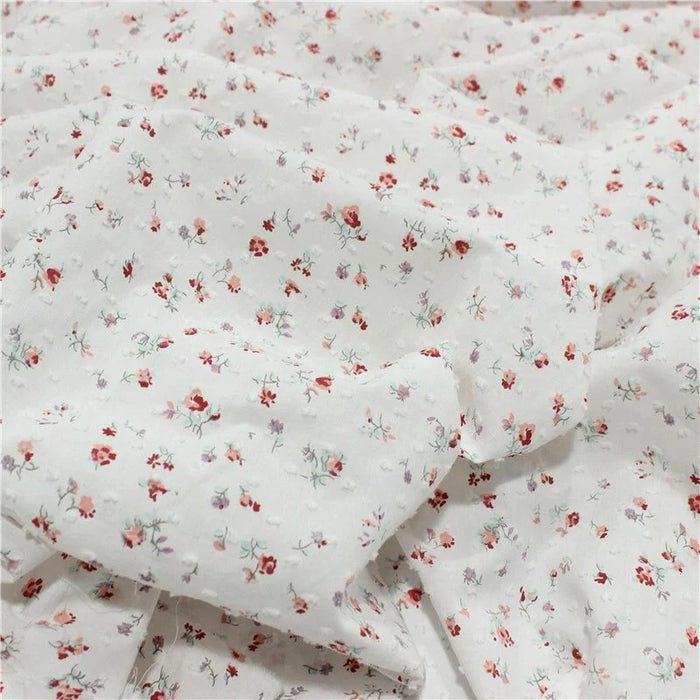 Un gros plan du Tissu plumetis rouge à motifs floraux au mètre de Longan Craft France montre un tissu vintage léger avec des motifs floraux et à pois, légèrement froissé pour un aspect charmant.