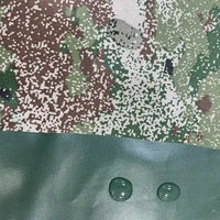 Gros plan sur le Tissu camouflage résistant à l'eau au mètre de Longan Craft France, montrant trois gouttes d'eau perlant sur la surface de la toile Oxford et une section de polyester vert solide, soulignant sa performance imperméable à l'extérieur.