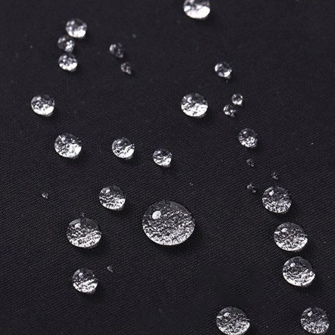 Des gouttes d'eau de différentes tailles s'éparpillent sur le Tissu gabardine imperméable au mètre noir et lisse de Longan Craft France, mettant en valeur ce textile résistant à l'eau, idéal pour les vêtements de travail.