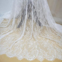 Dentelle Chantilly blanche au mètre de Longan Craft France : tissu dentelle français floral à bord festonné, parfait pour robes de mariée DIY, drapé sur fond beige avec motifs floraux délicats et détails raffinés.