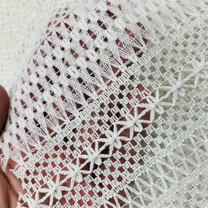Gros plan sur une main tenant le tissu dentelle en coton blanc au mètre de Longan Craft France, une dentelle jacquard ajourée aux motifs géométriques et floraux délicats, idéale pour DIY et confection de robes.