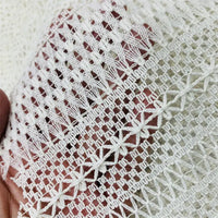 Gros plan sur une main tenant le tissu dentelle en coton blanc au mètre de Longan Craft France, une dentelle jacquard ajourée aux motifs géométriques et floraux délicats, idéale pour DIY et confection de robes.