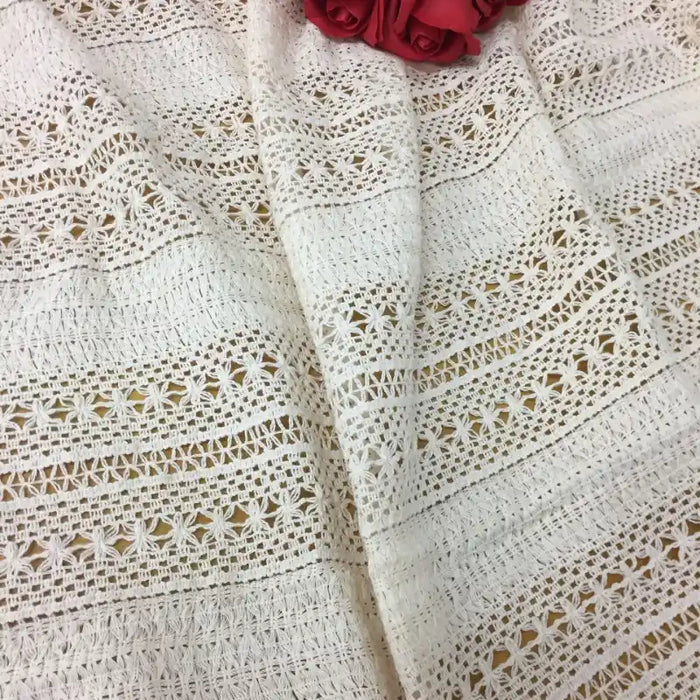 Gros plan sur le tissu dentelle en coton blanc au mètre-dentelle jacquard ajourée de Longan Craft France, aux motifs géométriques, drapé en douceur et orné de roses artificielles roses, parfait pour la confection de peignoirs.