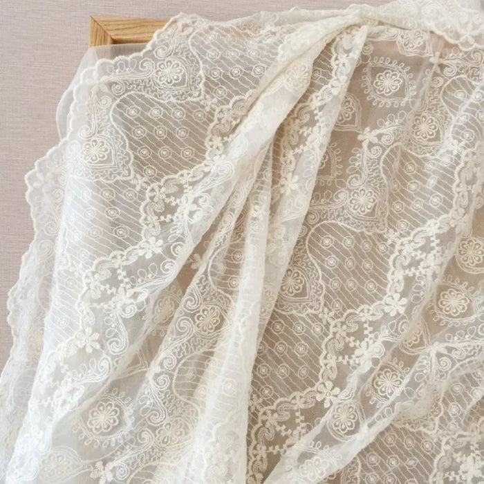 Le Tissu dentelle brodée florale blanche au mètre de Longan Craft France est élégamment présenté sur une planche en bois, idéal pour les projets de couture vintage ou de mariage.