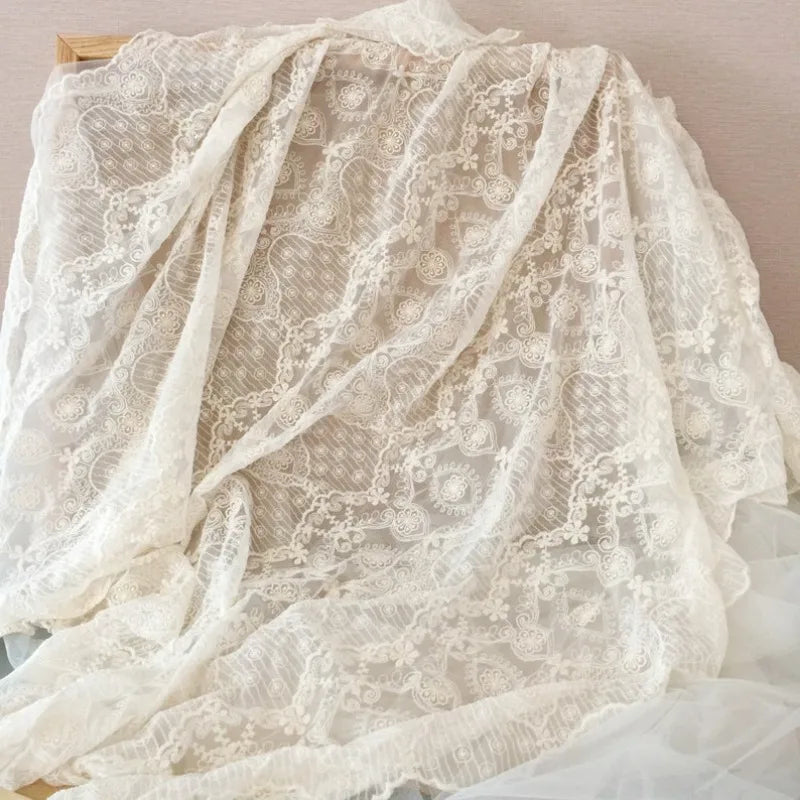 Une grande pièce de Tissu dentelle brodée florale blanche au mètre de Longan Craft France, présentant des motifs floraux vintage, est drapée sur un cadre en bois sur un fond neutre ; idéal pour la couture de mariage.