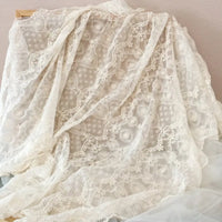 Une grande pièce de Tissu dentelle brodée florale blanche au mètre de Longan Craft France, présentant des motifs floraux vintage, est drapée sur un cadre en bois sur un fond neutre ; idéal pour la couture de mariage.