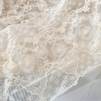 Gros plan sur le tissu dentelle brodée florale blanche au mètre de Longan Craft France : un tissu dentelle de mariage vintage et transparent avec de délicates broderies florales et géométriques, parfait pour les projets de couture.