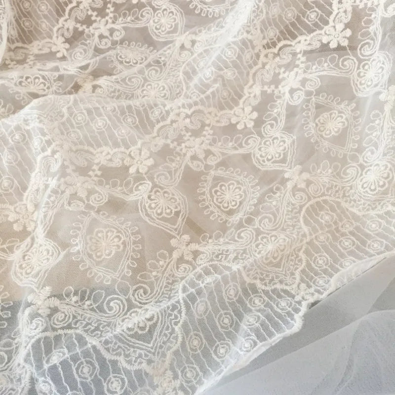 Gros plan sur le tissu dentelle brodée florale blanche au mètre de Longan Craft France : un tissu dentelle de mariage vintage et transparent avec de délicates broderies florales et géométriques, parfait pour les projets de couture.