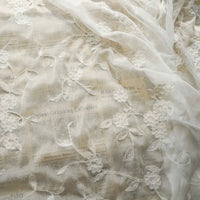 Le Tissu mousseline transparente brodée de fleurs au mètre de Longan Craft France présente une broderie florale transparente superposée à un journal imprimé, créant un contraste saisissant entre la dentelle délicate et le fond graphique.