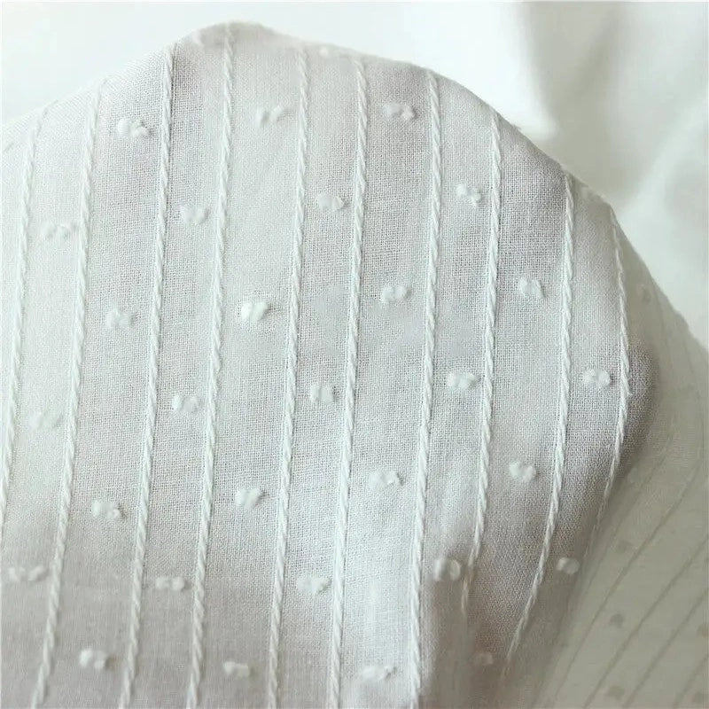 Gros plan sur le tissu jacquard à rayures blanches et plumetis au mètre de Longan Craft France, un tissu suisse transparent présentant des rayures blanches et des points en relief régulièrement espacés.