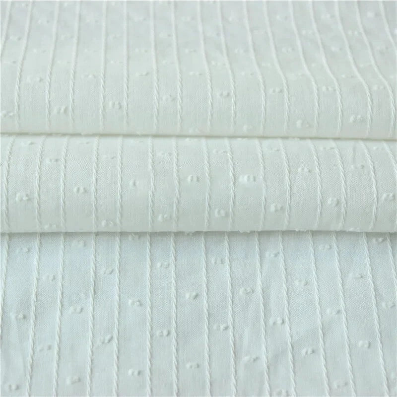 Gros plan sur le Tissu jacquard à rayures blanches et plumetis au mètre de Longan Craft France, qui présente des lignes verticales piquées et des points blancs régulièrement espacés sur un tissu suisse transparent.