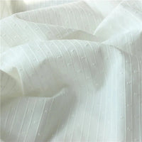 Gros plan sur le Tissu jacquard à rayures blanches et plumetis au mètre de Longan Craft France, un tissu suisse transparent avec des rayures blanches et des motifs en pointillés, montrant des plis doux et une texture délicate.