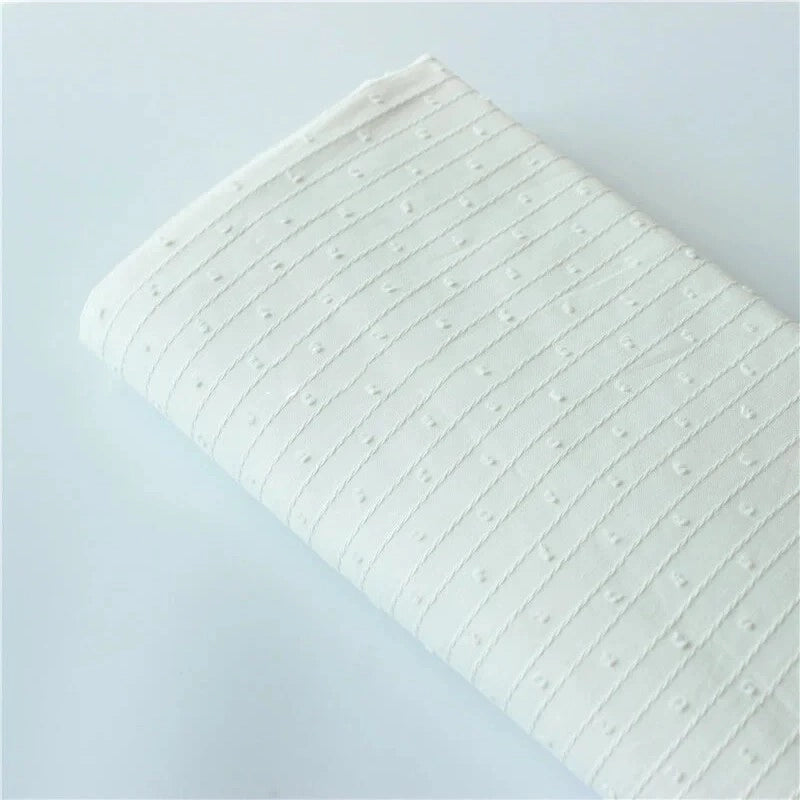 Une pièce pliée de Tissu jacquard à rayures blanches et plumetis au mètre de Longan Craft France, présentant un tissu suisse transparent avec des rayures blanches et des pois, présenté sur une surface claire et unie.