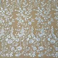 Le tulle brodé floral blanc au mètre de Longan Craft France présente d'élégantes broderies florales blanches dans un motif vertical symétrique sur un tulle marron clair - parfait pour la confection de vêtements de cérémonie élégants.