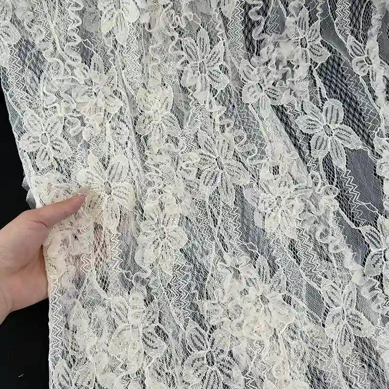 Une main tient Tissu en dentelle 3D au mètre de Longan Craft France, une dentelle française transparente aux motifs de fleurs et de feuilles complexes, idéale pour les jupes de printemps et d'été.