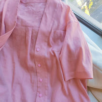 Une chemise boutonnée à manches courtes rose pâle avec une poche de poitrine est disposée près d'une fenêtre ensoleillée, inspirant votre prochaine création avec le Patron de chemise oversize femme à col en V PDF gratuit de Longan Craft France.