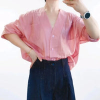 Vêtue d'une chemise à boutons rose pâle et ample fabriquée à partir du "Patron de chemise oversize femme à col en V | Téléchargement PDF gratuit" de Longan Craft France, la personne prend un selfie miroir avec un pantalon foncé taille haute et des accessoires.