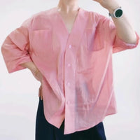 Une femme porte une chemise rose ample à col en V avec deux poches sur la poitrine et des manches trois quarts - idéal pour ceux qui recherchent le Patron de chemise oversize femme à col en V de Longan Craft France. S'associe bien avec un pantalon foncé et une montre intelligente.