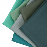 Des échantillons soigneusement empilés de Tissu gabardine de laine peignée et sergé laine-polyester de Longan Craft France sont présentés dans des coloris sarcelle, vert, gris et bleu - la gabardine résistante idéale pour les costumes sur mesure.