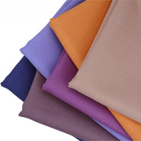 Une pile en forme d'éventail de gabardine de Longan Craft France (mélange de laine et de polyester), présentée en six couleurs unies - beige, orange, violet clair, violet foncé, lavande et bleu foncé - sur un fond blanc.