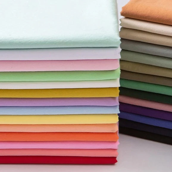 Une pile soigneusement empilée de Longan Craft France Tissu linon de coton tissé au mètre, disponible dans des teintes unies multicolores comme les pastels, les couleurs vives et les neutres, disposée horizontalement et verticalement sur une surface plane.