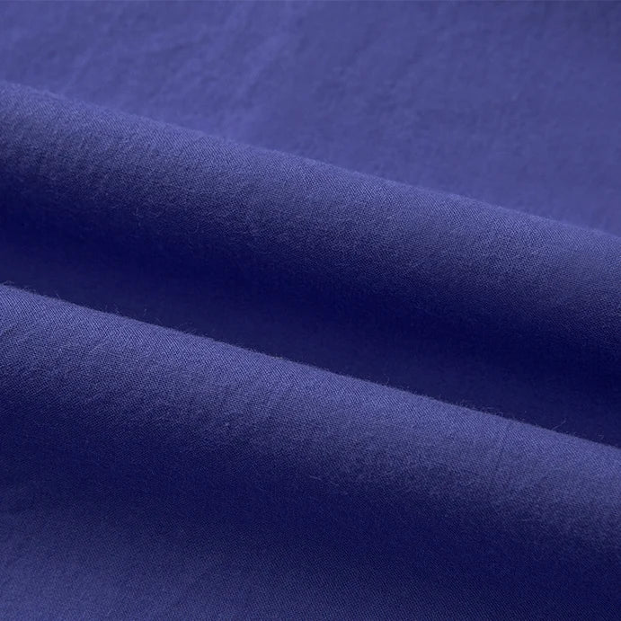 Gros plan sur le pliage du Tissu linon de coton tissé au mètre de Longan Craft France, mettant en valeur sa texture lisse, son aspect multicolore doux et les ombres légères le long des plis de coton à haute densité.