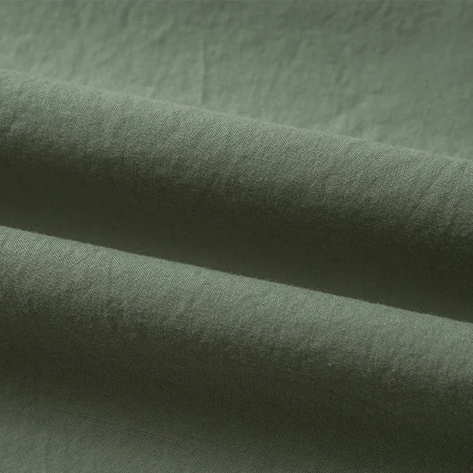 Gros plan sur le Tissu linon de coton tissé au mètre de Longan Craft France, qui présente un coton vert olive légèrement texturé avec des plis visibles, des ombres et des reflets subtils ; idéal comme doublure coton haute douceur.