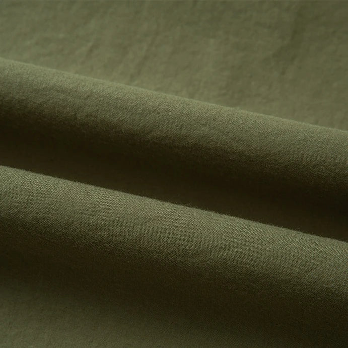 Gros plan sur le pliage du Tissu linon de coton tissé au mètre de Longan Craft France, en vert olive, dont la texture lisse et mate et le tissage visible sont parfaits pour les projets utilisant cette doublure multicolore de coton haute douceur.