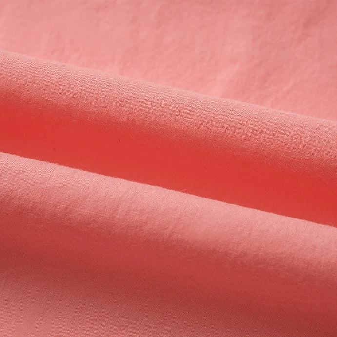 Gros plan sur le tissu linon de coton tissé au mètre de Longan Craft France, d'un rose corail uni, dont les plis délicats mettent en valeur la haute douceur et la texture moelleuse du linon de coton.