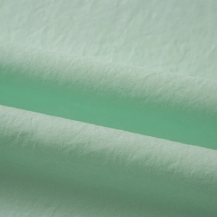 Gros plan sur le Tissu linon de coton tissé au mètre par Longan Craft France, un Coton linon multicolore vert clair avec une surface légèrement texturée et des plis horizontaux souples, idéal comme coton Doublure haute douceur.
