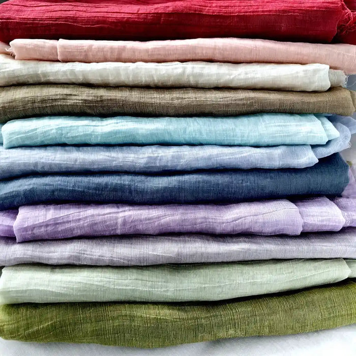 Une pile de Tissu lyocell froissé au mètre par Longan Craft France, avec un tissu lyocell léger, durable et respirant dans des tons dégradés de rouge, rose, blanc, beige, bleu, violet et vert.