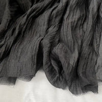 Gros plan sur le Tissu lyocell noir froissé au mètre de Longan Craft France, qui présente des lignes verticales texturées et se drape sur une surface légère - un textile lyocell léger et respirant, idéal pour les hauts.
