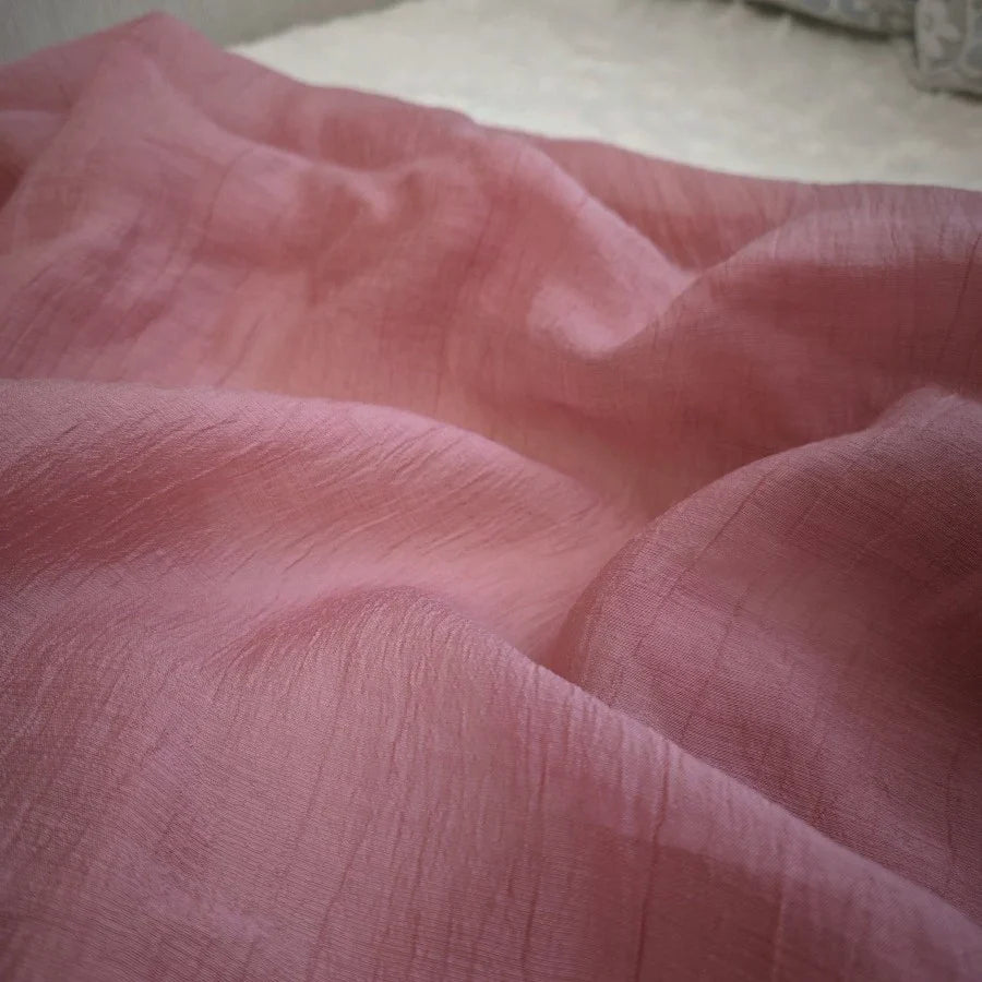 Un gros plan du Tissu lyocell froissé au mètre de Longan Craft France montre un tissu lyocell rose doux et froissé avec une surface légèrement texturée et des plis délicats. Ce textile léger et durable est idéal pour les hauts respirants.
