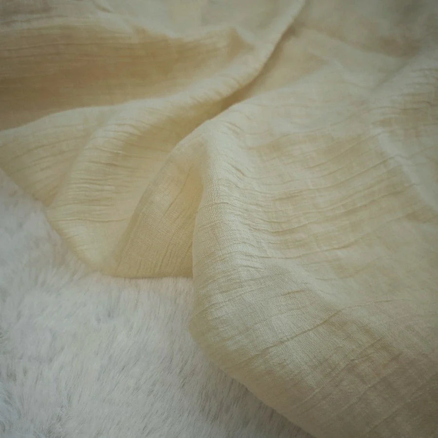 Gros plan sur un Tissu lyocell froissé au mètre, beige clair, de Longan Craft France, montrant des plis visibles sur une surface douce et blanche ressemblant à de la fourrure. Ce textile lyocell léger et durable est respirant, idéal pour les hauts.