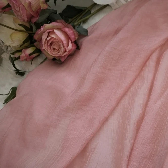 Un tissu lyocell transparent rose pâle de Longan Craft France est présenté à côté d'un petit bouquet de roses artificielles. Ce textile respirant et résistant, vendu au mètre, est idéal pour la confection de hauts légers.