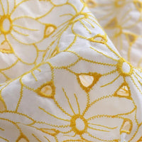 Gros plan sur le tissu brodé ajouré œillet jaune au mètre de Longan Craft France : tissu 100 % coton présentant une broderie florale jaune, des détails de découpe, une texture légère et légèrement transparente avec de délicats accents jaunes.