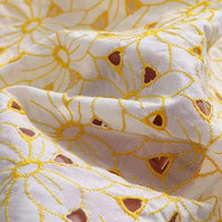 Gros plan sur le Tissu brodé ajouré œillet jaune au mètre de Longan Craft France, mettant en valeur son 100% coton, sa broderie florale jaune, ses détails découpés et sa texture complexe.