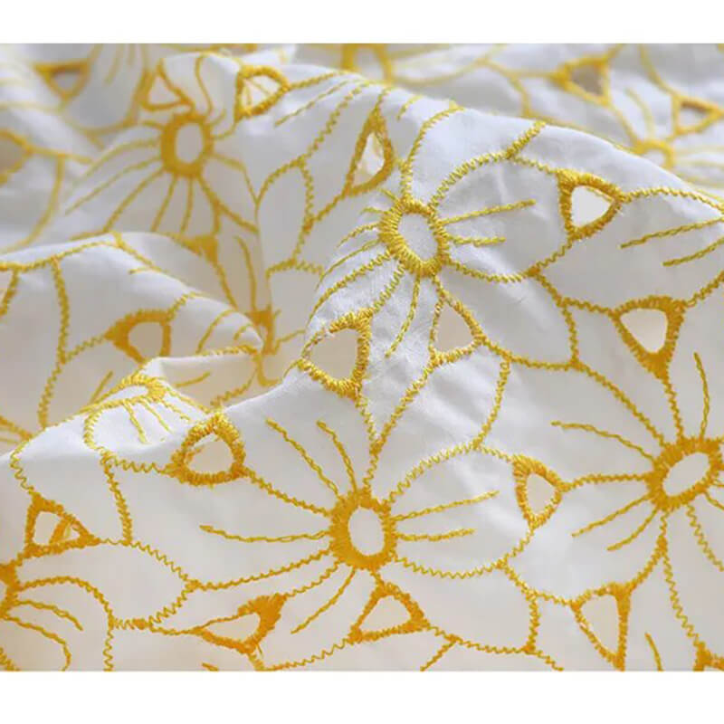 Gros plan sur le Tissu brodé ajouré œillet jaune au mètre de Longan Craft France, un tissu 100 % coton brodé d'œillets floraux jaunes ; l'image bien éclairée met en valeur sa texture et ses détails délicats.