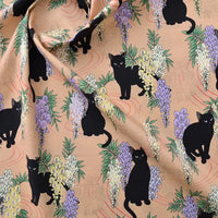 Tissu popeline coton stretch imprimé floral chat Longan Craft France au mètre, idéal pour DIY, patchwork, robes et chemises. Motifs chats noirs parmi glycines violettes/jaunes sur fond beige clair ; légères ondulations par endroits.