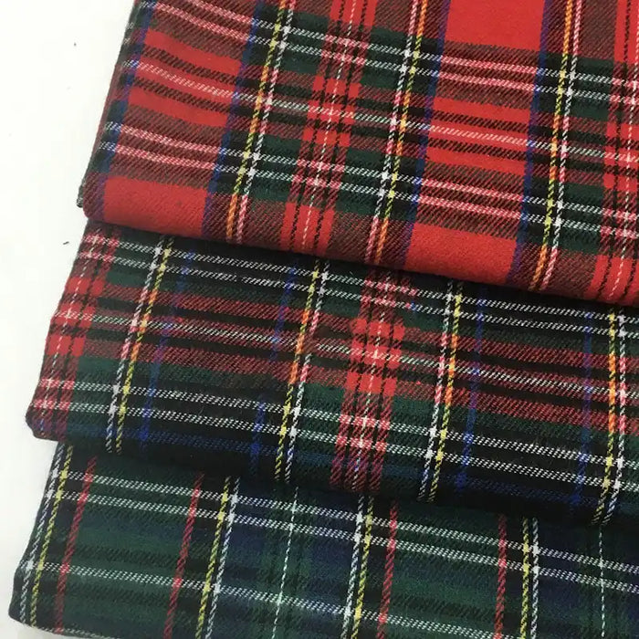 Trois pièces pliées de tissu écossais de Noël en flanelle de Longon Craft France, à rayures écossaises rouges, vertes, bleues, jaunes et blanches, sont empilées sur une surface blanche. Parfait pour les travaux de couture et de bricolage festifs.