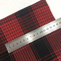 Une règle métallique mesurant de 1 à 20 cm est posée en diagonale sur du tissu rouge et noir Tissu flanelle à carreaux de Noël au mètre de Longon Craft France, un tissu polyester-coton confortable pour la couture festive, les robes, les chemises et les travaux manuels.