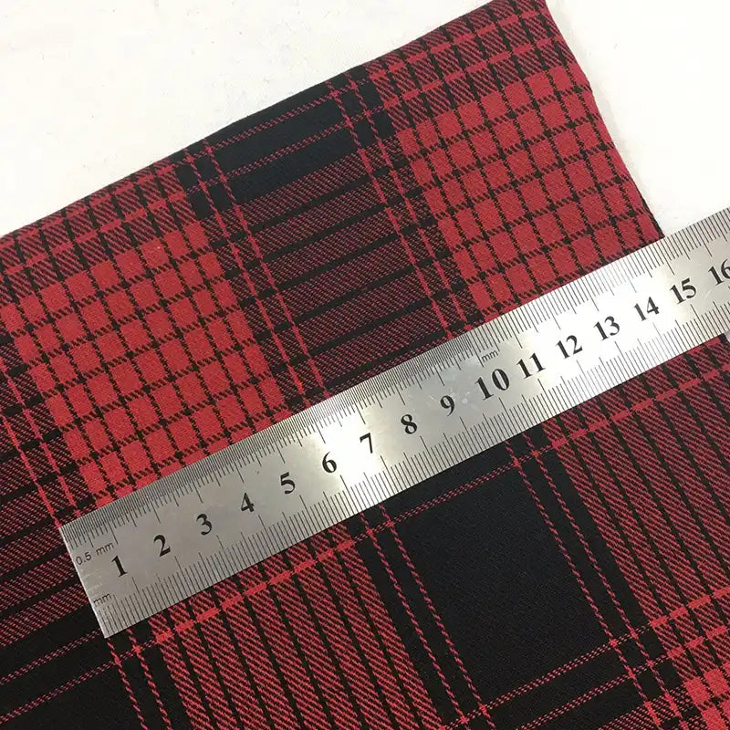 Une règle métallique mesurant de 1 à 20 cm est posée en diagonale sur du tissu rouge et noir Tissu flanelle à carreaux de Noël au mètre de Longon Craft France, un tissu polyester-coton confortable pour la couture festive, les robes, les chemises et les travaux manuels.