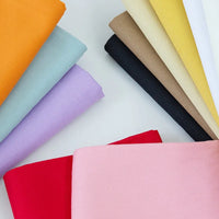 Une sélection de Tissu jean coloré 7,5 oz au mètre de Longan Craft France - 100 % coton denim sergé pour les jeans colorés - disposés en demi-cercle avec orange, bleu clair, lavande, rouge, rose, noir, marron, jaune, beige et blanc sur une surface blanche.