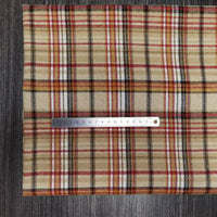 Une règle en argent de 15 cm repose horizontalement sur un Tissu en flanelle à carreaux colorés de Longon Craft France, un tissu polyester-coton ultra-confortable pour l'automne, présenté sur une surface en bois foncé.