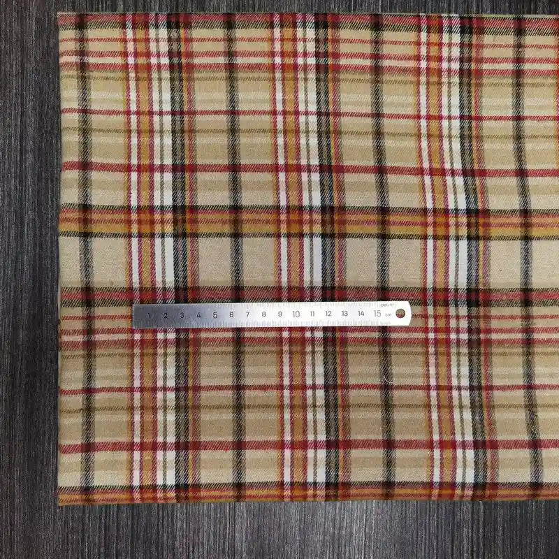 Une règle en argent de 15 cm repose horizontalement sur un Tissu en flanelle à carreaux colorés de Longon Craft France, un tissu polyester-coton ultra-confortable pour l'automne, présenté sur une surface en bois foncé.