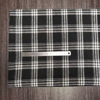 Une règle argentée est posée sur un tissu écossais coloré de Longon Craft France, en polyester-coton ultra-doux, parfait pour l'automne, étalé sur une surface en bois sombre.