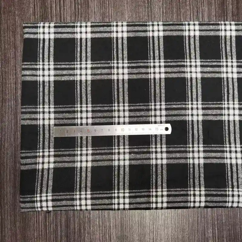 Une règle argentée est posée sur un tissu écossais coloré de Longon Craft France, en polyester-coton ultra-doux, parfait pour l'automne, étalé sur une surface en bois sombre.